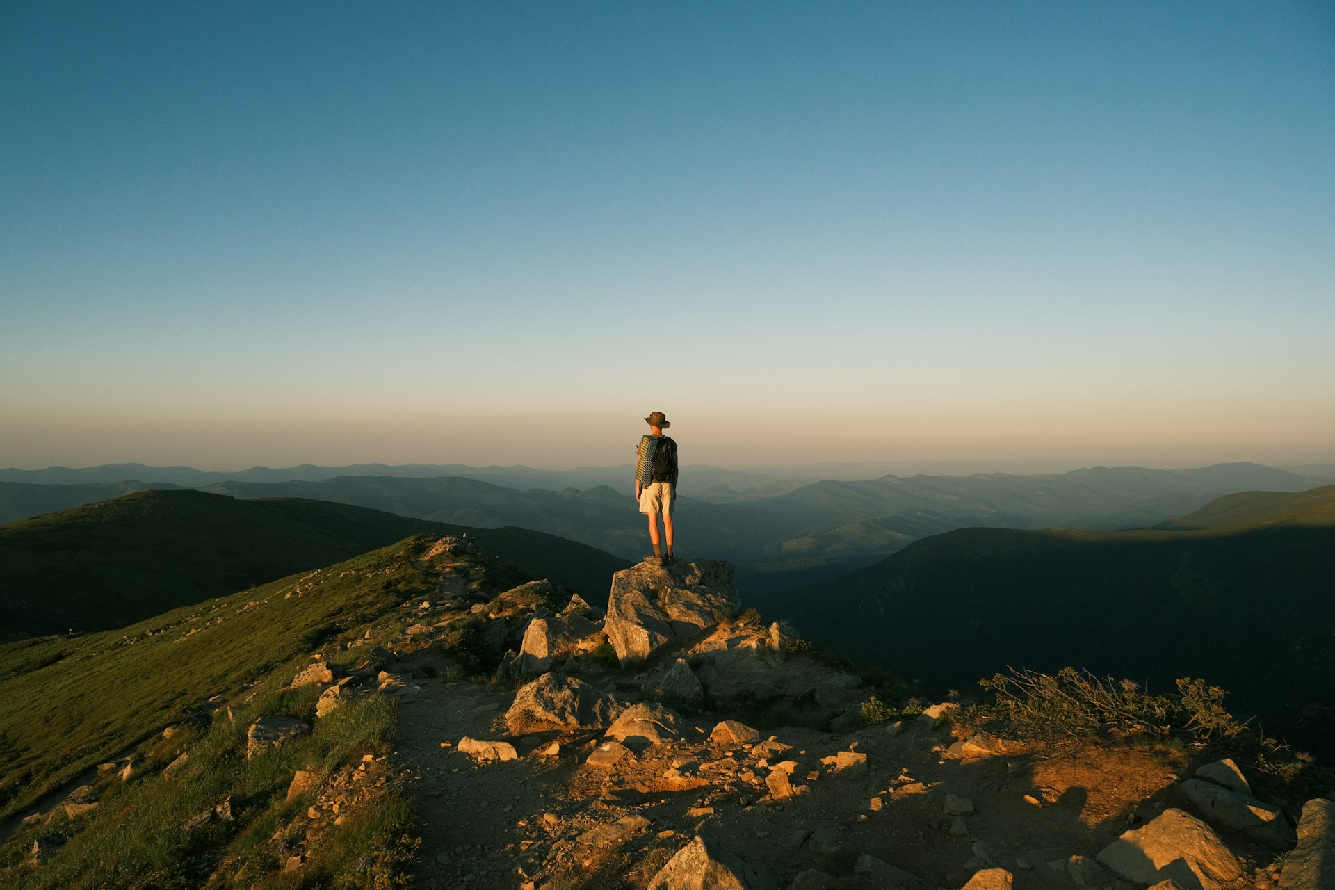 Person standing on a rocky mountain peak at sunset.
