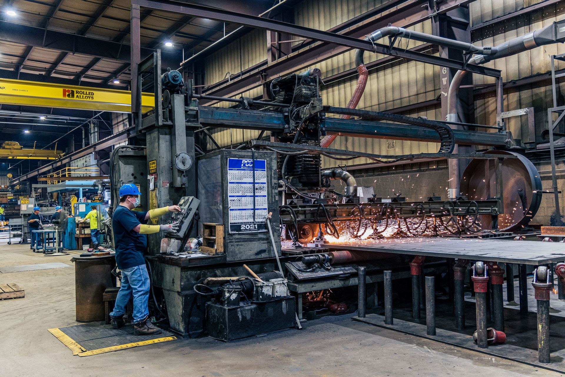 A worker wearing safety gear operates machinery in a busy manufacturing factory